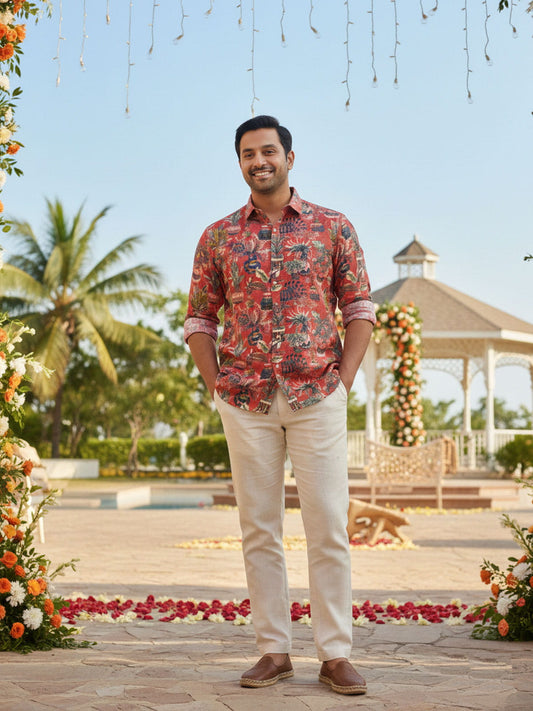 Man in a Bright Maroon Tropical Print Privee Paris Shirt standing in a decorated outdoor setting with palm trees and a gazebo.